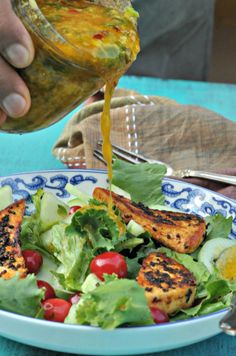 someone pouring dressing onto a salad in a blue and white bowl on top of a table