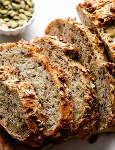 sliced loaf of bread sitting on top of a cutting board next to two bowls filled with seeds