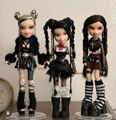 three dolls are standing next to each other on a table with black and white accessories