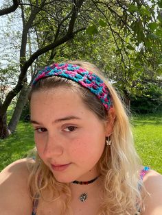 a young woman wearing a colorful headband sitting in the grass next to a tree