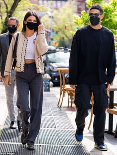 a woman wearing a face mask walks down the street with two men in black suits