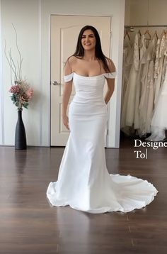 a woman standing in front of a mirror wearing a white wedding dress with off the shoulder sleeves