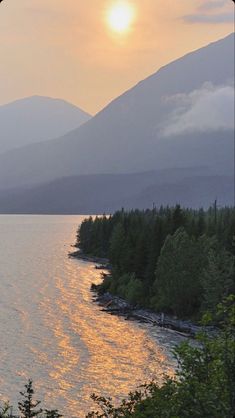 the sun is setting over water with mountains in the background and trees on either side