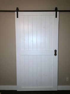 a white barn door with black hardware on the top and bottom bars in an empty room