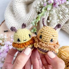 two tiny crocheted animals are being held by someone's hands with flowers in the background