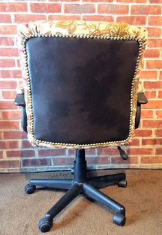 a black leather chair sitting in front of a brick wall with gold trimmings