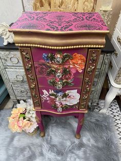 a pink and gold painted chest of drawers with flowers on the top, sitting on a fur rug