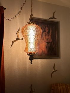 a lamp hanging from the side of a wall next to a painting and bird sculptures