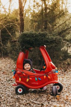 a small child in a red car with christmas lights on it's roof and trees growing out of the top