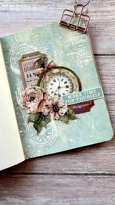 an open book with flowers and a clock on it, sitting on a wooden table