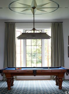 a pool table in front of a window with drapes on the windowsills