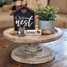 a small house shaped sign sitting on top of a wooden table next to a potted plant