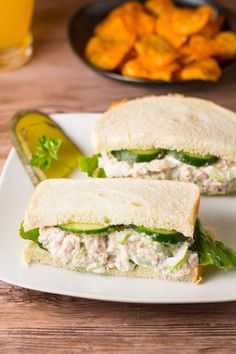 two halves of a chicken salad sandwich on a plate with pickles next to it