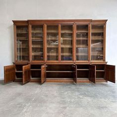 a large wooden cabinet with glass doors and drawers on the front, in an empty room