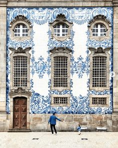 a person standing in front of a building with blue and white tiles on the wall