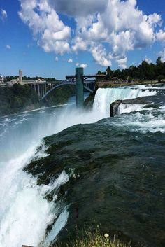 the water is rushing over the edge of the falls and under the bridge that goes to the other side