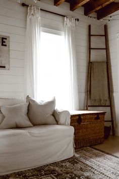 a white couch sitting in front of a window next to a rug and wooden ladder