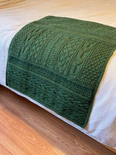 a green blanket sitting on top of a bed next to a white pillow and wooden floor