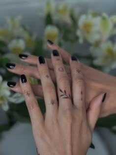 two hands with black and white nail polish holding each other's fingers in front of flowers