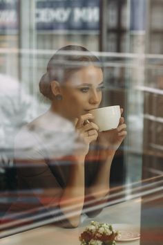 a woman sitting at a table with a cup in her hand looking out the window