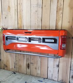 an orange pickup truck parked in front of a wooden wall