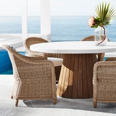 there is a table and chairs on the patio by the ocean with flowers in a vase