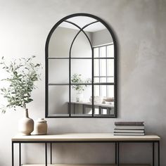 an arched mirror on the wall above a table with a vase and books next to it