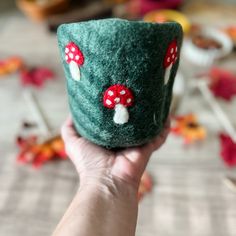 a hand holding a green cup with red mushrooms on it