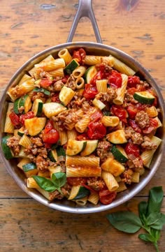 a skillet filled with pasta and meat on top of a wooden table next to leaves