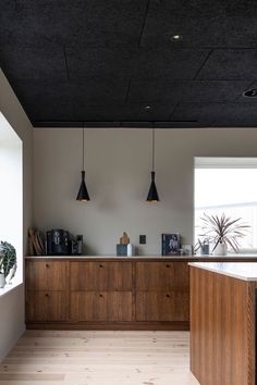 an empty kitchen with wooden cabinets and hanging lights above the countertop, along with potted plants