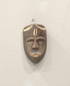 a metal mask hanging on the wall next to a white wall with a light bulb