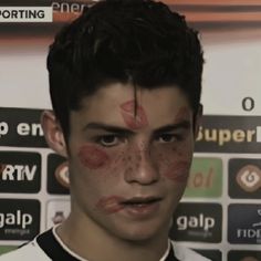 a young man with his face painted red and black, standing in front of a wall