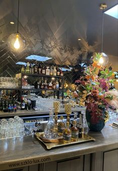 a bar with lots of liquor bottles and glasses on the top shelf, next to a vase filled with flowers