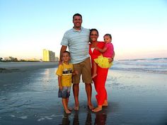 a man, woman and two children standing on the beach