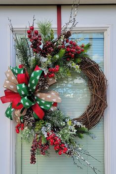 a christmas wreath hanging on a door with red and green bows, pine cones, evergreens and berries