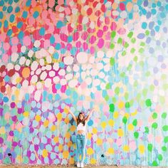 a woman standing in front of a colorful wall with lots of circles painted on it