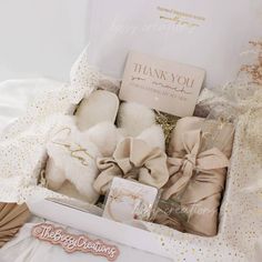 a box filled with lots of white items on top of a bed next to a thank card