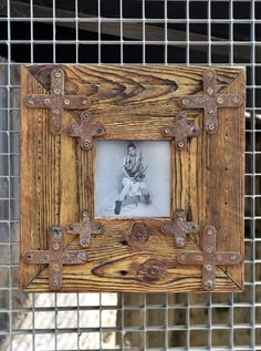 an old wooden frame with metal straps hanging on a wire mesh fence behind it is a photo of a young boy