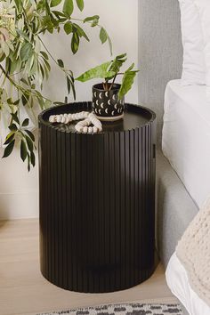 a plant sits on top of a round table in front of a bed with white sheets