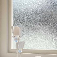 a candle and two glasses on a table in front of a frosted glass window