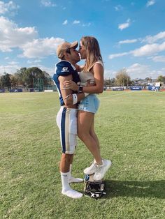 a man and woman are kissing on the football field while wearing white shorts and blue jerseys