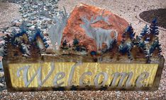 a metal welcome sign sitting on top of a gravel covered ground next to a rock