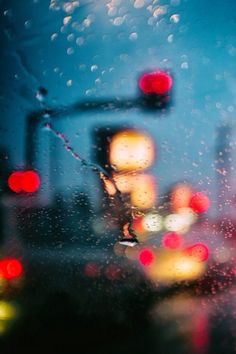 rain drops on the windshield of a car as traffic lights are seen in the background