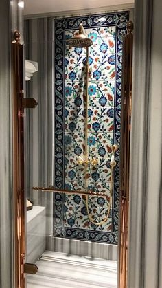 an ornate shower in a white bathroom with blue and gold tiles on the wall behind it