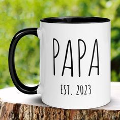 a black and white coffee mug sitting on top of a tree stump with the word papa printed on it