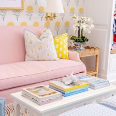 a living room with a pink couch and white coffee table in front of a yellow flowered wall