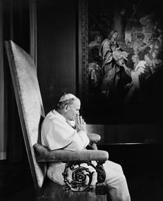 a black and white photo of a man sitting in a chair with his hand on his face