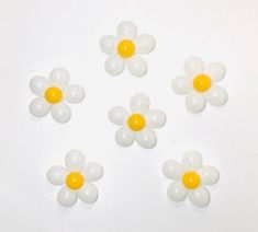 five white and yellow balloons are arranged in the shape of daisies on a white surface