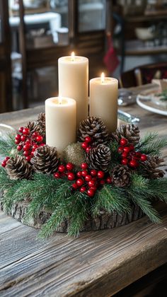 three candles are sitting on a table with pine cones, berries and holly wreaths