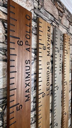 three wooden rulers are hanging on the wall next to a stone wall with words written on them